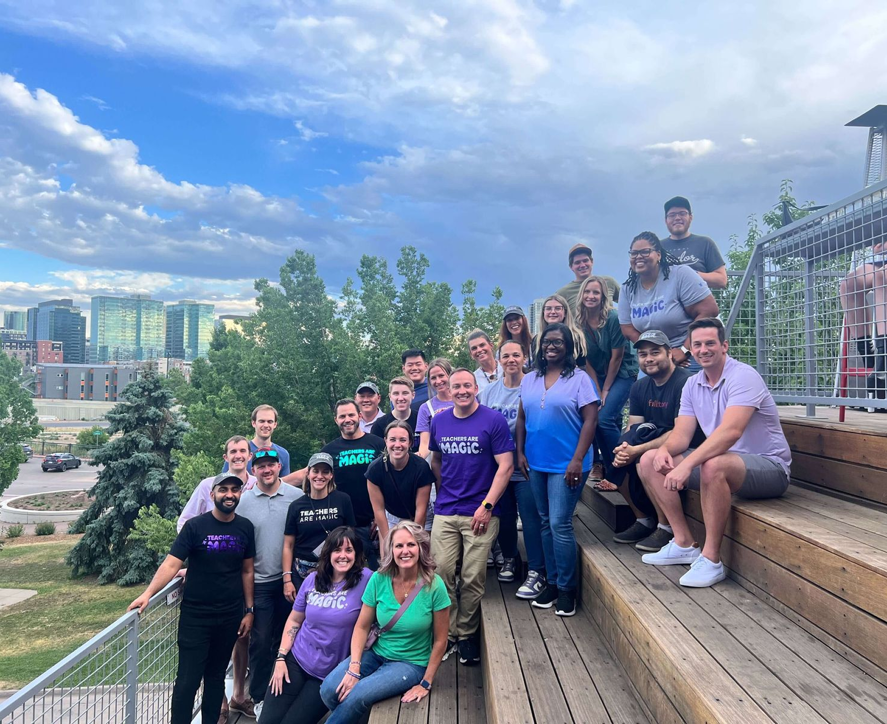 Group of MagicSchool employees posing for a group photo on wooden stairs with mountain in the background